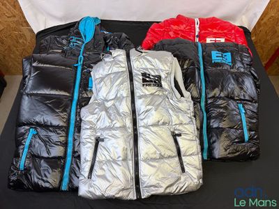 Plusieurs vestes sont alignées sur une table devant un fond blanc.