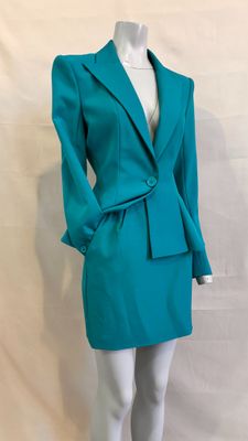 Le mannequin porte un tailleur-jupe de couleur bleu sarcelle.