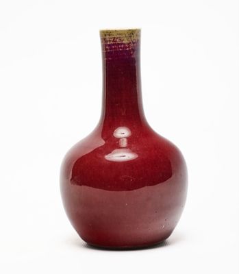 un vase rouge posé sur une surface blanche