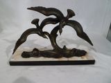 une statue en bronze représentant trois oiseaux, posée sur un socle en marbre