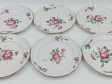 six assiettes ornées de roses, posées sur une table blanche