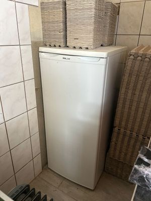 un réfrigérateur blanc dans un coin de la pièce, sur lequel est empilée une pile de cartons