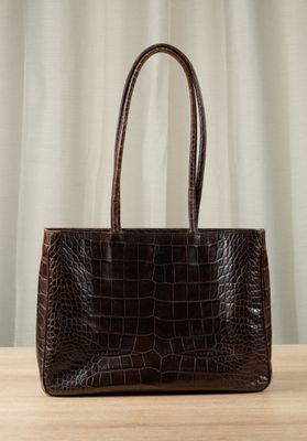 brown alligator skin handbag on a wooden table with curtains in the background