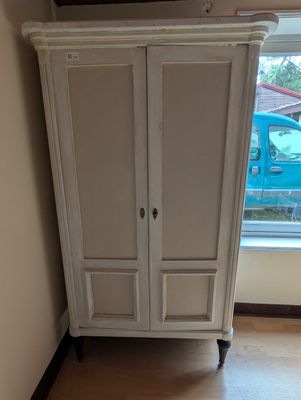 une armoire blanche dans un coin de la pièce, près d'une fenêtre