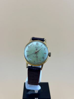 une photo d'une montre posée sur un socle, sur une surface blanche