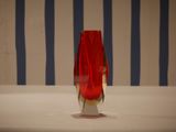 a red vase sitting on a table with a striped wall behind it