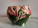 a green vase with pink flowers on it on a table