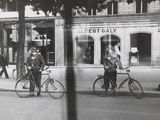 black and white photograph of two men riding bicycles on a city street