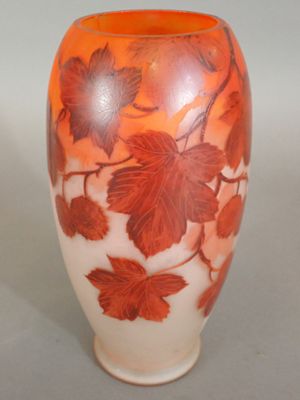an orange vase with leaves on it sitting on a table