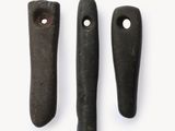 trois pierres noires percées de trous, posées sur une surface blanche