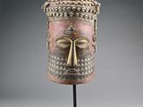 un masque en bois posé sur un socle, sur fond gris