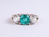 a close up of an emerald and diamond ring on a white surface