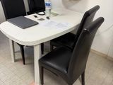 une table blanche avec des chaises noires et un ordinateur portable posé dessus