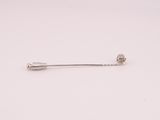 a silver pin with a flower on it sitting on a white surface