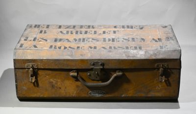 une vieille valise posée sur une table, sur laquelle est accrochée une pancarte