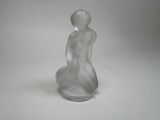 une figurine en verre représentant une femme assise sur une surface blanche