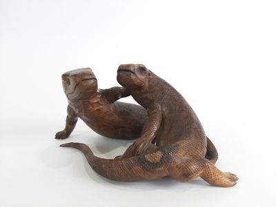 une paire de loutres en bronze, assises sur le dos sur une surface blanche
