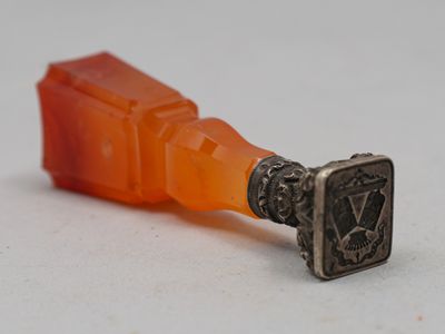une bouteille orange munie d'une poignée métallique, posée sur une surface blanche