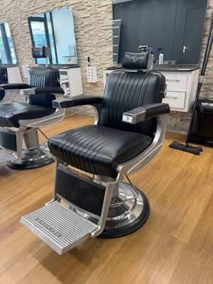 fauteuil de coiffeur noir et chromé devant un miroir dans un salon de coiffure pour hommes