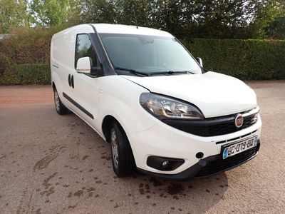 La camionnette blanche est garée sur un parking près d'une haie.