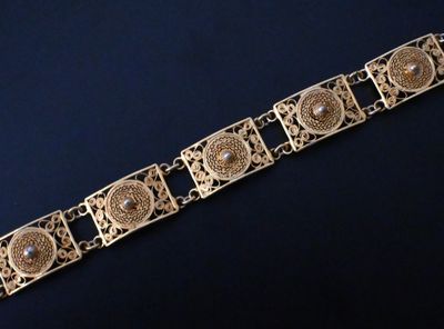 gros plan d'un bracelet en or sur une surface noire