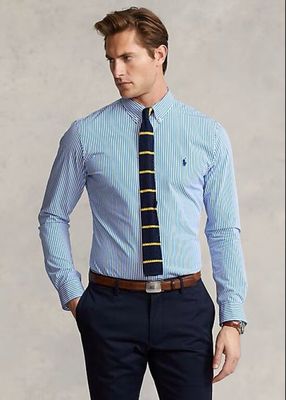 a man in a blue shirt and tie standing with his hands in his pockets