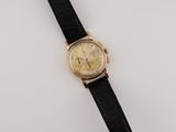 a gold and black watch with a black strap on a white surface