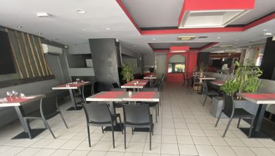 Dans un restaurant aux murs rouges, des tables et des chaises sont alignées.