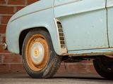 an old blue car parked in front of a brick wall