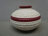 un vase blanc au crochet, muni d'un couvercle rouge, posé sur une table