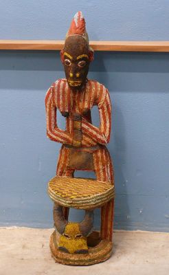 une statue en bois représentant un homme assis sur un tabouret
