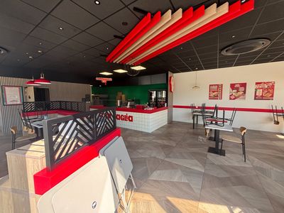 Dans un restaurant aux touches de rouge et de blanc, les tables et les chaises sont alignées.