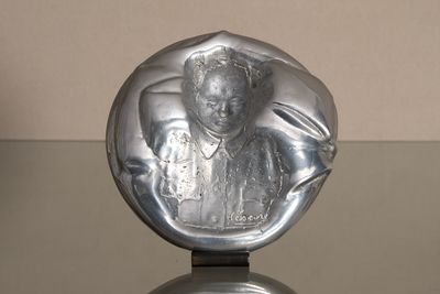 une sculpture en argent représentant une femme assise sur une table en verre
