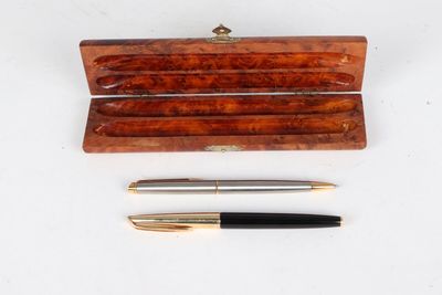 deux stylos et un étui en bois posés sur une surface blanche