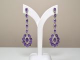 des boucles d'oreilles violettes et blanches posées sur un présentoir blanc, sur une table blanche