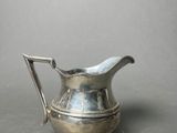 an antique silver plated pitcher with a handle on a gray surface