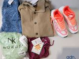 Plusieurs paires de chaussures, un pull, un jean, une paire de baskets et un sac de vêtements sont posés sur une table.