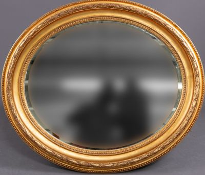 un miroir ovale avec un cadre doré posé sur une surface grise