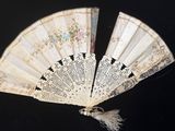 une image représentant un éventail blanc orné de motifs floraux et de pompons