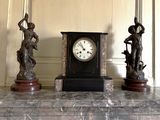 trois statues et une horloge posées sur une table en marbre
