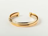 a gold cuff bracelet with a curved design on a white background