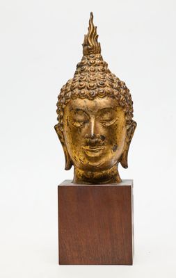 une image représentant une tête de Bouddha dorée posée sur un socle en bois