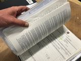someone holding a book on top of a wooden table in an office