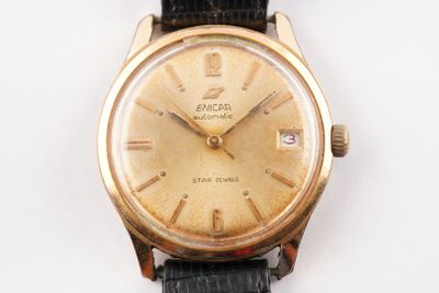 une montre en or avec un bracelet noir posée sur un fond blanc