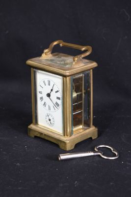 une petite horloge dorée avec une clé sur fond noir