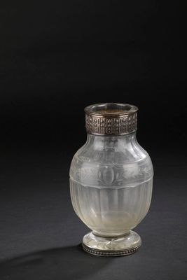 un vieux vase en verre muni d'un couvercle en argent, posé sur une surface noire