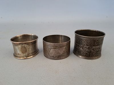 trois serviettes anciennes en argent, ornées de motifs, posées sur une table