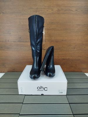 une paire de bottes noires à talons hauts posée sur une boîte blanche
