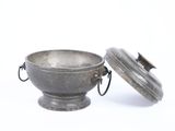 a small metal bowl with a lid on a white surface