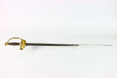 un gros plan d'une épée à la poignée dorée posée sur une surface blanche